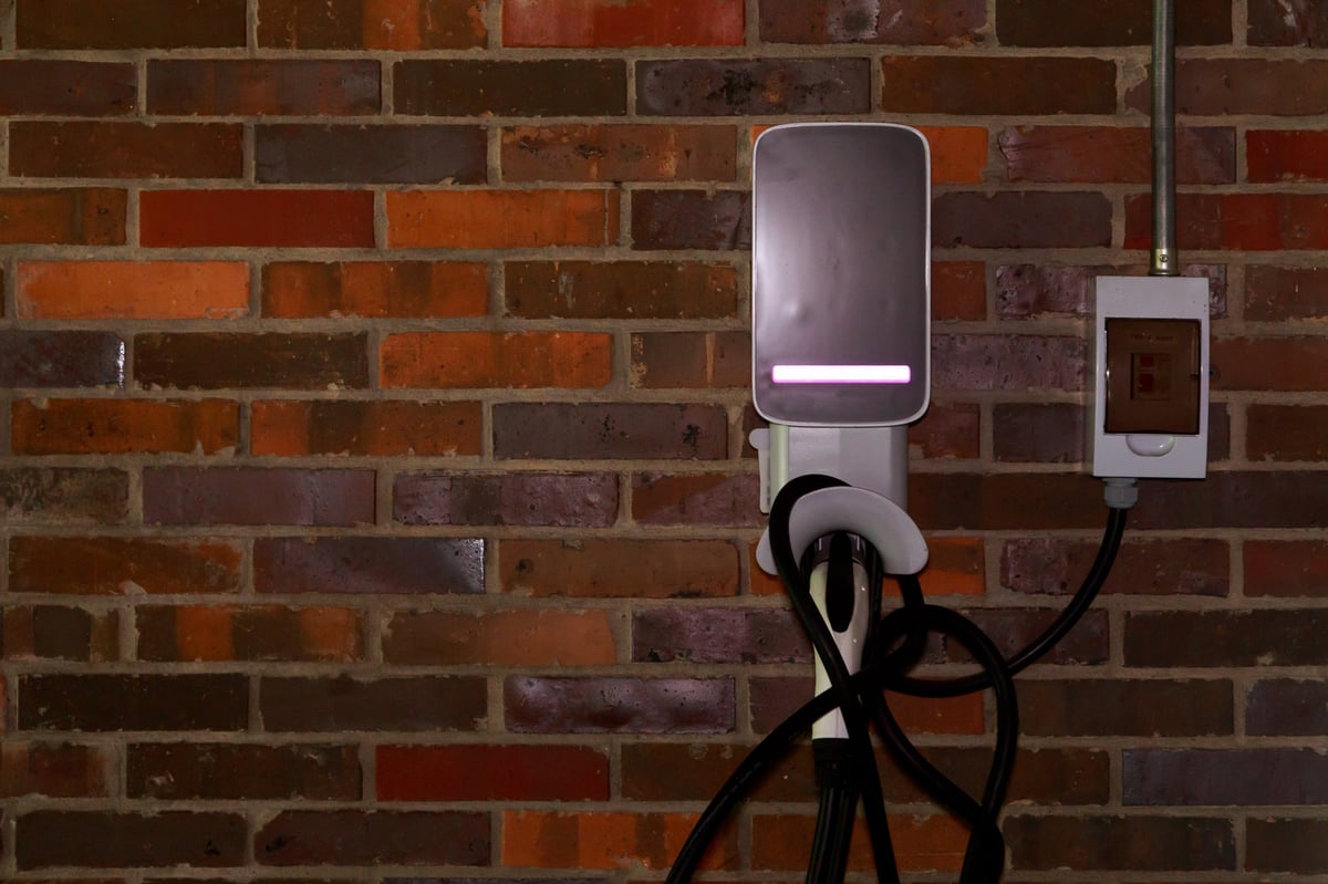 Electric vehicle wallbox charger with cable mounted on a red brick wall indoors