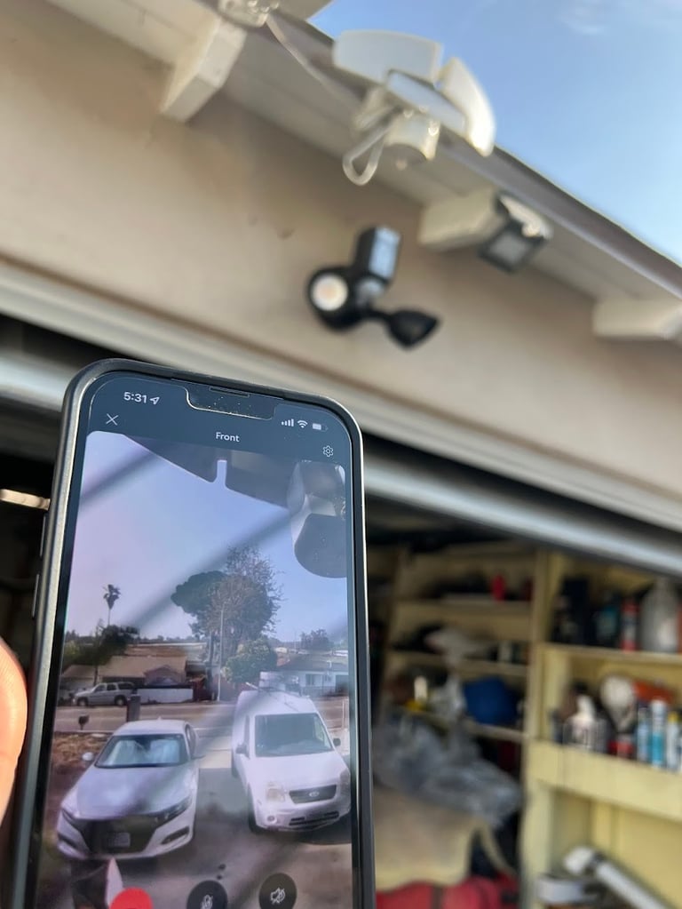 Smartphone displaying live camera feed of driveway with outdoor security camera mounted on garage
