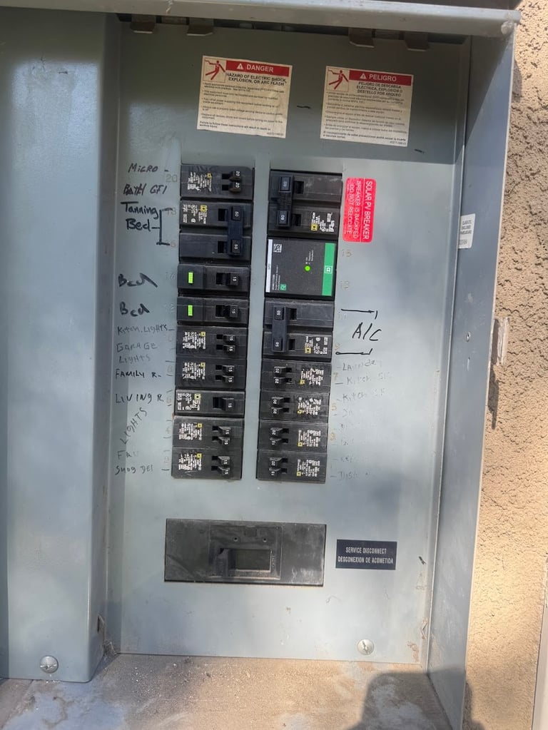 Electrical breaker panel box mounted on wall with multiple circuit breakers, warning labels, and handwritten notes