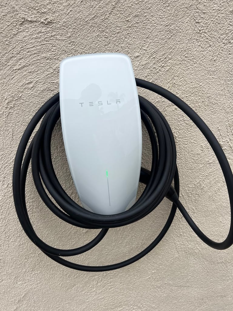 White Tesla EV charging connector with coiled black cable on wall