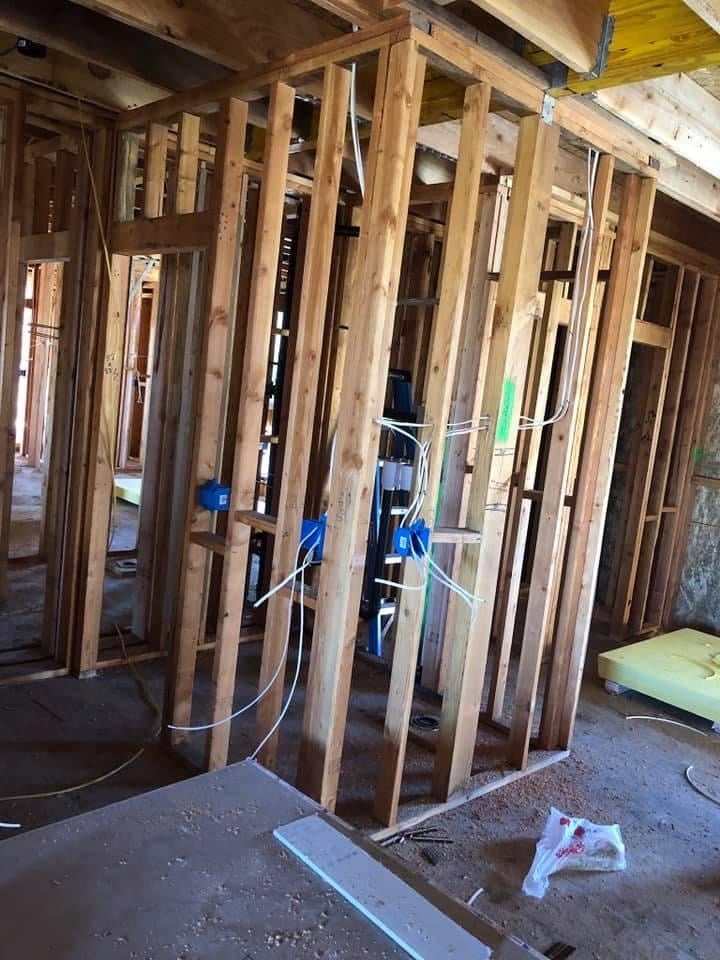 Interior framing of a house under construction with wooden studs, electrical wiring, and building materials