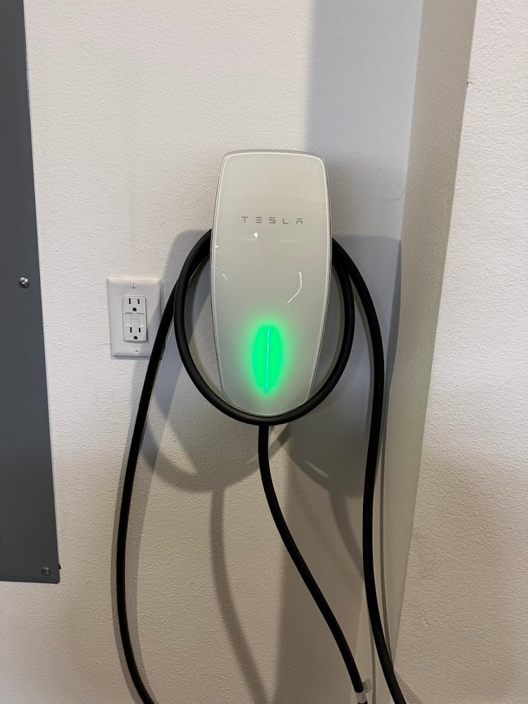 Tesla wall-mounted electric vehicle charging station with green illuminated indicator light and black charging cable