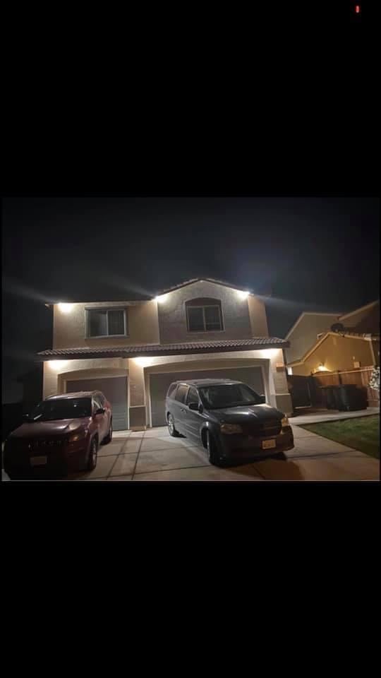 Two-story house at night with exterior lighting, driveway with two parked vehicles