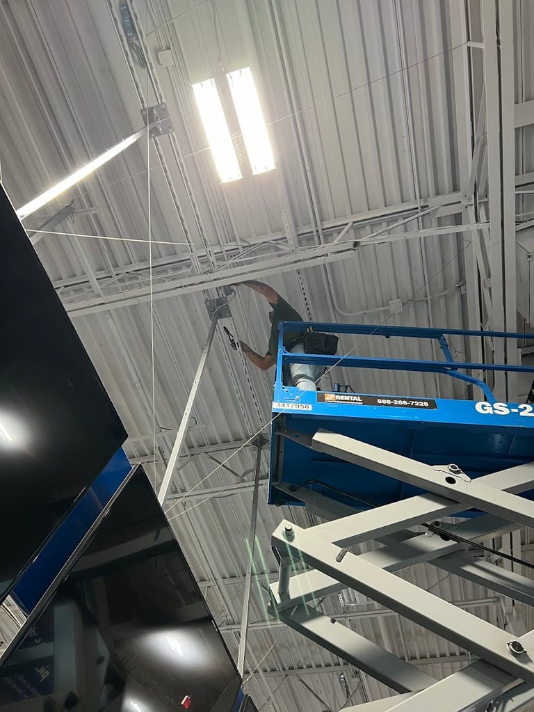 Worker on blue scissor lift installing lighting fixture in industrial warehouse