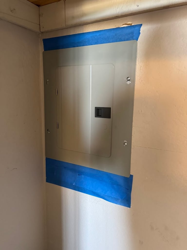 Electrical panel mounted on wall with blue painters tape applied for protection during renovation