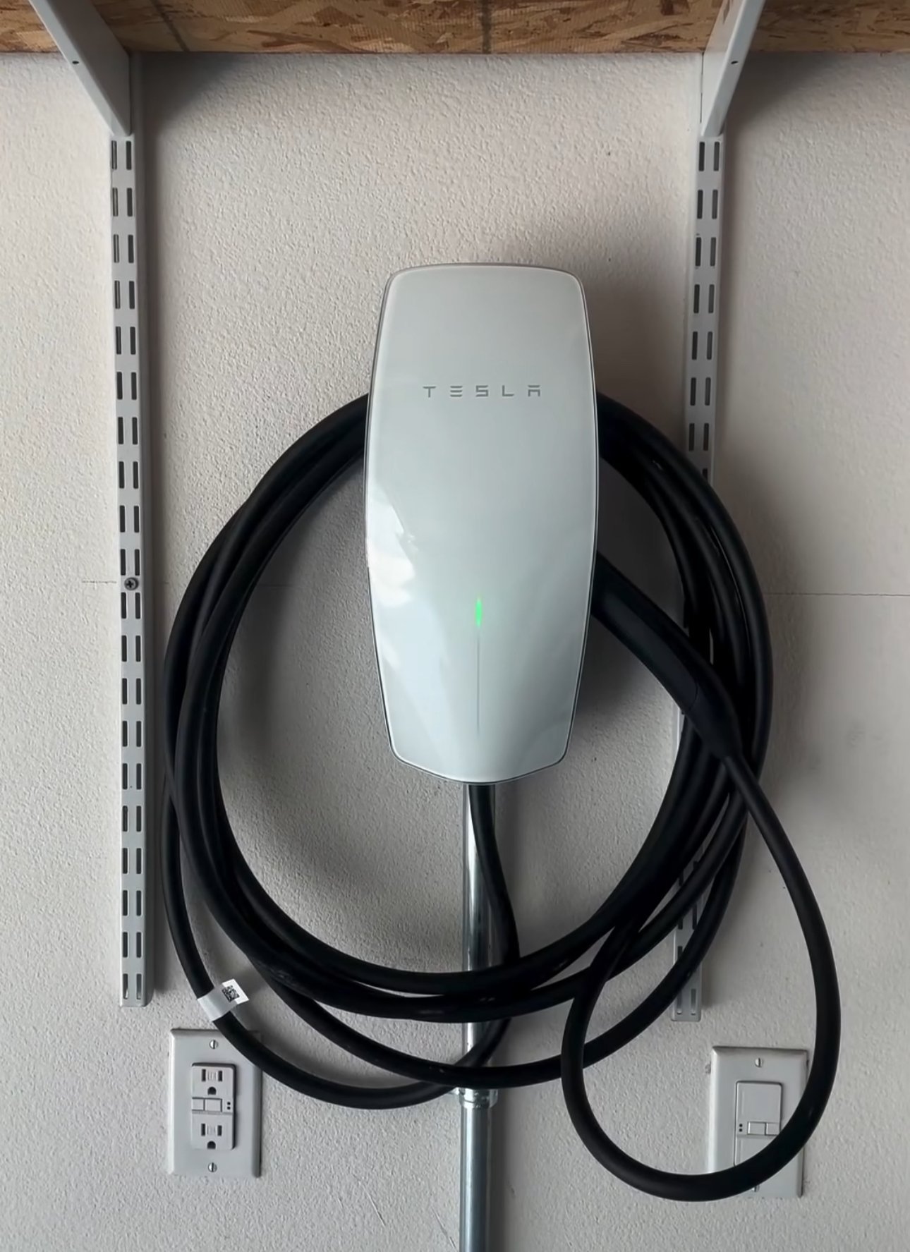 White Tesla electric vehicle charger mounted on wall with coiled black charging cable and outlets below