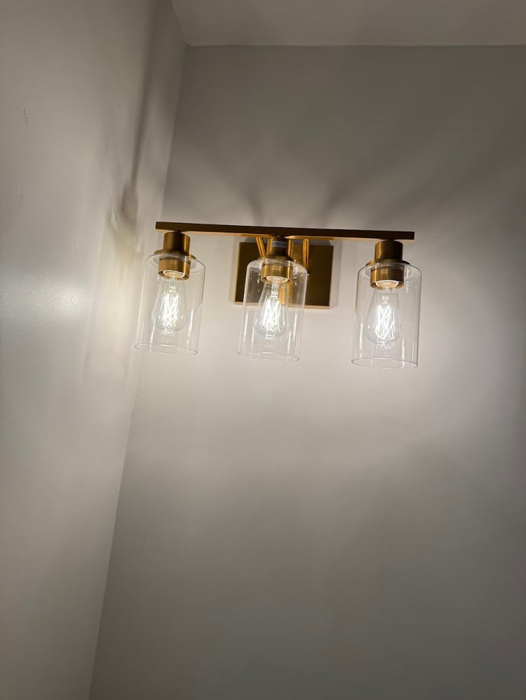 Modern brass vanity light fixture with three clear glass cylindrical shades